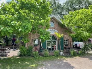 Gemütliches Backsteingebäude mit grünem Biergarten unter schattigen Bäumen